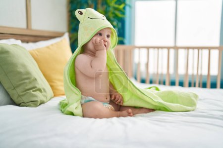 Foto de Adorable bebé caucásico con divertida toalla chupando dedo en el dormitorio - Imagen libre de derechos