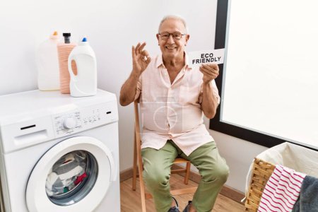 Téléchargez les photos : Senior homme faisant la lessive tenant papier respectueux de l'environnement faire ok signe avec les doigts, sourire geste amical excellent symbole - en image libre de droit
