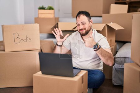 Photo for Plus size hispanic man with beard moving to a new home doing video call smiling happy and positive, thumb up doing excellent and approval sign - Royalty Free Image