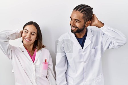 Foto de Young hispanic doctors standing over white background smiling confident touching hair with hand up gesture, posing attractive and fashionable - Imagen libre de derechos