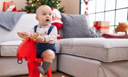 Photo for Adorable caucasian baby playing with reindeer rocking by christmas tree at home - Royalty Free Image