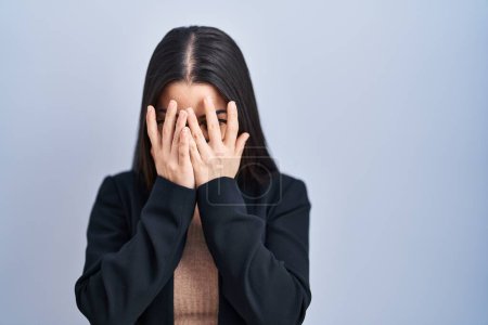 Jeune femme brune debout sur fond bleu avec une expression triste couvrant le visage des mains tout en pleurant. concept de dépression. 