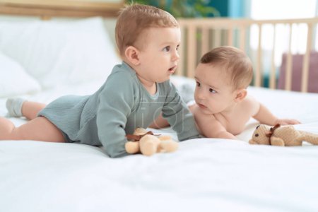 Photo for Two toddlers lying on bed playing with teddy bear at bedroom - Royalty Free Image
