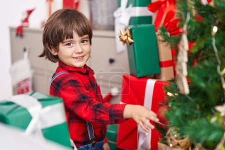 Foto de Adorable niño sonriendo confiado decorando árbol de Navidad en casa - Imagen libre de derechos