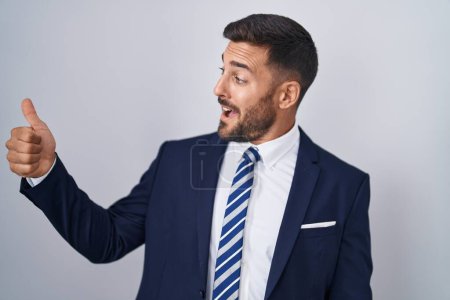 Foto de Hombre hispano guapo vistiendo traje y corbata luciendo orgulloso, sonriendo haciendo un gesto hacia un lado - Imagen libre de derechos