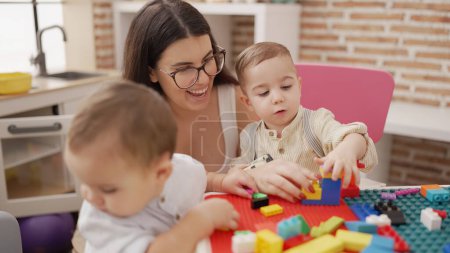 Foto de Profesores y estudiantes de preescolar jugando con bloques de construcción sentados en la mesa en el jardín de infantes - Imagen libre de derechos