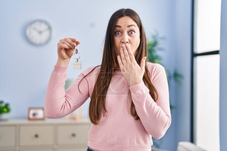 Photo for Young brunette woman holding keys of new home covering mouth with hand, shocked and afraid for mistake. surprised expression - Royalty Free Image