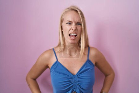 Photo for Young caucasian woman standing over pink background angry and mad screaming frustrated and furious, shouting with anger. rage and aggressive concept. - Royalty Free Image