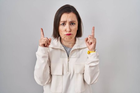 Photo for Middle age hispanic woman standing over isolated background pointing up looking sad and upset, indicating direction with fingers, unhappy and depressed. - Royalty Free Image