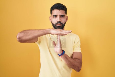 Téléchargez les photos : Hispanic man with beard standing over yellow background doing time out gesture with hands, frustrated and serious face - en image libre de droit