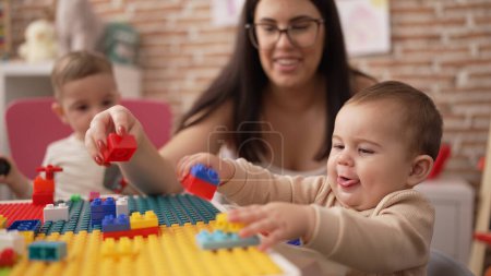 Foto de Profesores y estudiantes de preescolar jugando con bloques de construcción sentados en la mesa en el jardín de infantes - Imagen libre de derechos