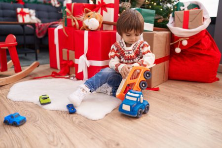 Foto de Adorable toddler playing with truck toy sitting on floor by christmas tree at home - Imagen libre de derechos