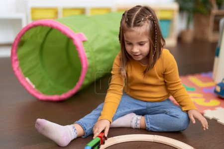 Foto de Adorable chica hispana jugando con coches juguete sentado en el suelo en el jardín de infantes - Imagen libre de derechos
