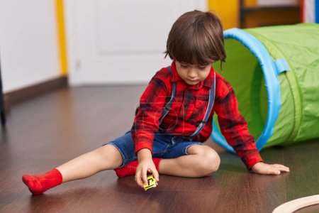 Téléchargez les photos : Adorable tout-petit jouant avec des voitures jouet assis sur le sol à la maison - en image libre de droit