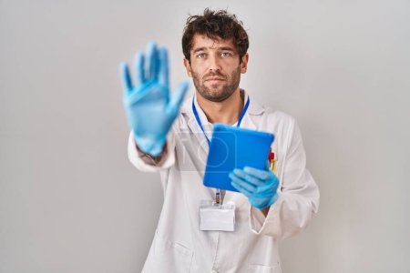 Foto de Hispanic scientist man working with tablet with open hand doing stop sign with serious and confident expression, defense gesture - Imagen libre de derechos
