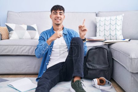 Photo for Young hispanic man sitting on the floor studying for university smiling and looking at the camera pointing with two hands and fingers to the side. - Royalty Free Image