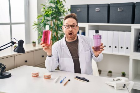 Photo for Middle age caucasian dentist man holding mouthwash for fresh breath afraid and shocked with surprise and amazed expression, fear and excited face. - Royalty Free Image