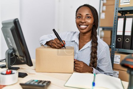 Téléchargez les photos : Femme afro-américaine e-commerce travailleur d'affaires en utilisant l'écriture informatique sur le paquet au bureau - en image libre de droit