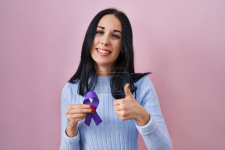 Téléchargez les photos : Hispanic woman holding purple ribbon awareness smiling happy and positive, thumb up doing excellent and approval sign - en image libre de droit