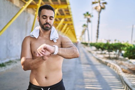 Photo for Hispanic man working out outdoors on a sunny day looking calories on smartwatch - Royalty Free Image