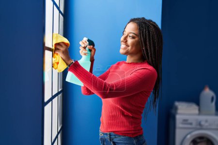 Foto de Mujer afroamericana sonriendo confiada ventana de limpieza en casa - Imagen libre de derechos
