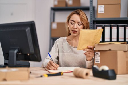 Téléchargez les photos : Jeune femme ecommerce busines travailleur écriture sur ordinateur portable holding package au bureau - en image libre de droit