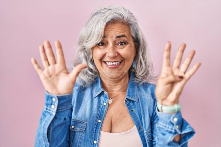 Foto de Mujer de mediana edad con el pelo gris de pie sobre el fondo rosa que muestra y señala hacia arriba con los dedos número nueve mientras sonríe confiado y feliz. - Imagen libre de derechos