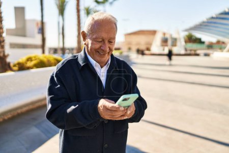 Foto de Hombre mayor sonriendo confiado usando el teléfono inteligente en el parque - Imagen libre de derechos
