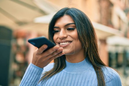 Téléchargez les photos : Jeune femme hispanique envoyant un message vocal avec smartphone à la ville - en image libre de droit
