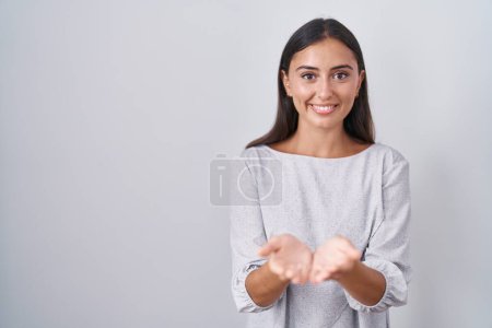 Photo for Young hispanic woman standing over white background smiling with hands palms together receiving or giving gesture. hold and protection - Royalty Free Image
