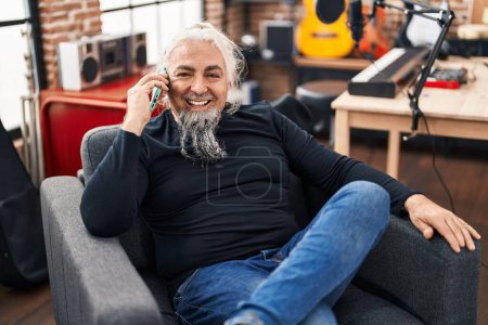 Photo for Middle age grey-haired man musician talking on smartphone sitting on chair at music studio - Royalty Free Image