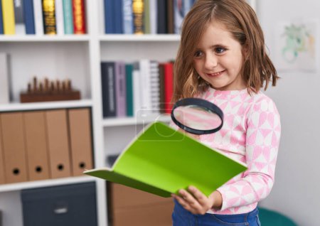 Téléchargez les photos : Adorable hispanique fille élève lecture livre à l'aide de loupe à l'école de la bibliothèque - en image libre de droit