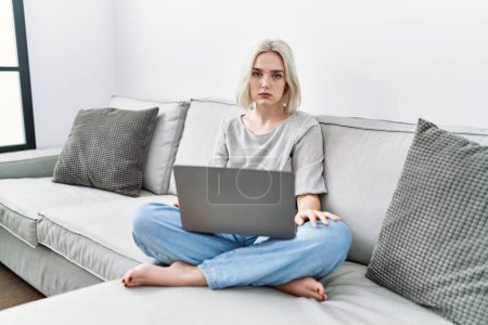 Photo for Young caucasian woman using laptop at home sitting on the sofa skeptic and nervous, frowning upset because of problem. negative person. - Royalty Free Image
