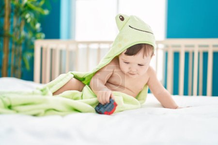 Téléchargez les photos : Adorable bébé caucasien portant une serviette drôle de jouer avec la voiture à la chambre - en image libre de droit