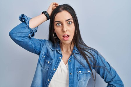 Photo for Hispanic woman standing over blue background in shock face, looking skeptical and sarcastic, surprised with open mouth - Royalty Free Image