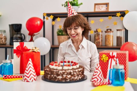 Foto de Middle age woman celebrating birthday holding big chocolate cake looking positive and happy standing and smiling with a confident smile showing teeth - Imagen libre de derechos