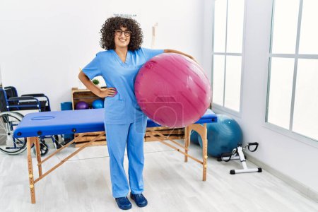 Téléchargez les photos : Jeune femme du Moyen-Orient portant un uniforme de physiothérapeute tenant ballon en forme à la clinique - en image libre de droit