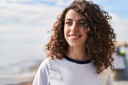 Téléchargez les photos : Young hispanic woman smiling confident looking to the side at seaside - en image libre de droit