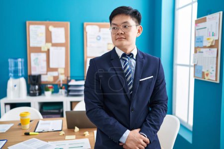 Téléchargez les photos : Jeune homme d'affaires chinois debout avec une expression détendue au bureau - en image libre de droit
