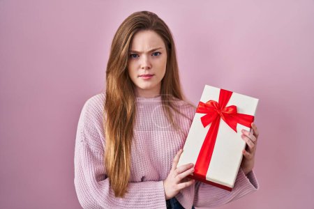 Photo for Young caucasian woman holding gift skeptic and nervous, frowning upset because of problem. negative person. - Royalty Free Image