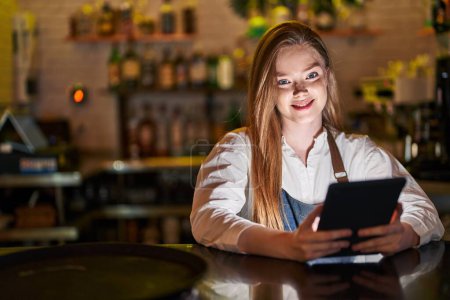 Téléchargez les photos : Young caucasian woman waitress smiling confident using touchpad at restaurant - en image libre de droit