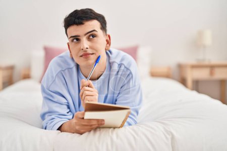 Téléchargez les photos : Young non binary man writing on notebook lying on bed - en image libre de droit