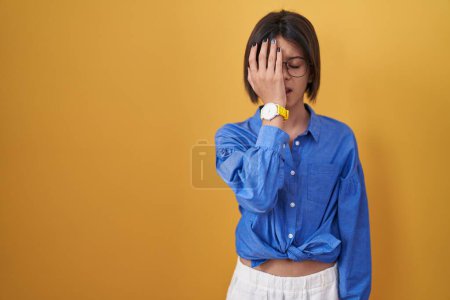 Photo for Young girl standing over yellow background yawning tired covering half face, eye and mouth with hand. face hurts in pain. - Royalty Free Image