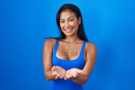 Foto de Hispanic woman standing over blue background smiling with hands palms together receiving or giving gesture. hold and protection - Imagen libre de derechos