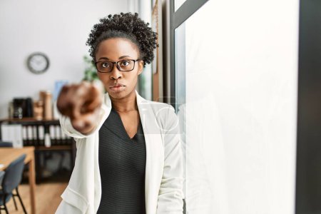 Téléchargez les photos : Femme d'affaires africaine travaillant au bureau pointant du doigt la caméra et à vous, geste confiant regardant sérieux - en image libre de droit