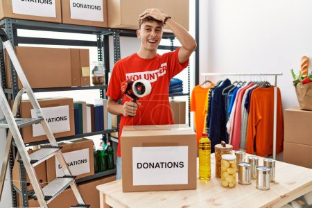 Téléchargez les photos : Young caucasian volunteer man packing donations box at charity center stressed and frustrated with hand on head, surprised and angry face - en image libre de droit