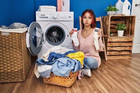 Photo for Young caucasian woman doing laundry holding socks puffing cheeks with funny face. mouth inflated with air, catching air. - Royalty Free Image
