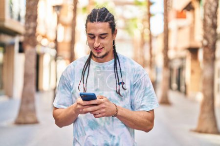 Téléchargez les photos : Jeune homme souriant confiant en utilisant smartphone à la rue - en image libre de droit