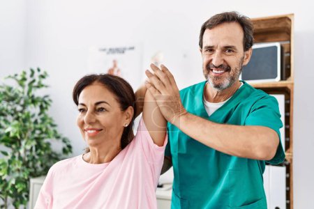 Foto de Hombre y mujer de mediana edad sonriendo confiado brazo de estiramiento que tiene sesión de rehabilitación en la clínica de fisioterapia - Imagen libre de derechos