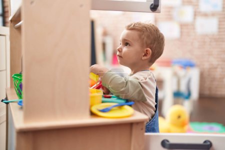 Téléchargez les photos : Adorable tout-petit jouant avec la cuisine de jeu debout à la maternelle - en image libre de droit